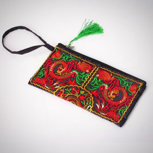 The image is of the Double Dragon Embroidered Clutch. Features: The material is for interior and exterior is cotton, the style is a day clutch, the closure is a zipper, the size is approximately 15cm x 27cm, no straps, interior compartment, embroidered pattern, green tassel on the end of the zipper.